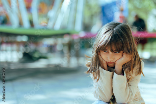 Sad Girl Sitting Facing Away the Trampoline in Amusement Park. Unhappy solitary child feeling lonely and being disappointed