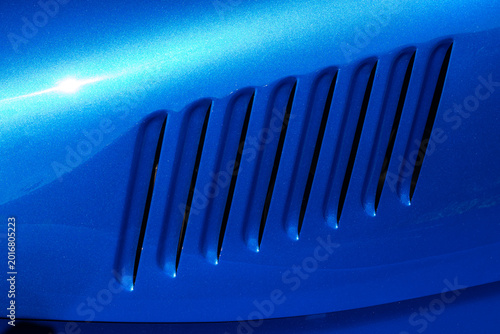 Close-up of a series of louvres pressed into a vivid blue metallic car panel, casting deep shadows against the sparkling paintwork