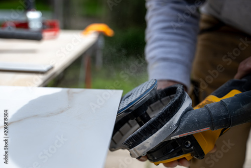 Worker is polishing tile and making the edge of a ceramic tile with an electric grinder on a workbench during a home project. Close up