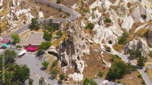 Goreme, Nevsehir, Turkey. The Monastery of Nuns and Monks, a towering rock-hewn monastic complex with multiple carved levels and cave openings, aerial drone view over the eroded Cappadocian valley. A