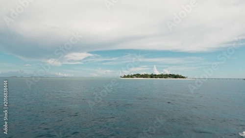 Wide shot of a lush Fiji island and long wooden pier seen from a boat on the water
