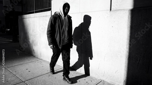 Inside the mind of a person facing depression concept. A lone figure walks in shadows on a city sidewalk.