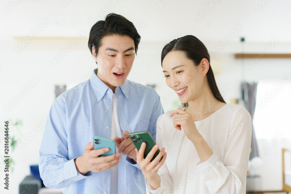 Fototapeta premium リビングでスマホを持って会話する若い日本人セレブカップル