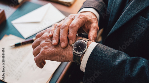 Senior Businessman Checking Watch On Wrist At Desk With Letters And Pen