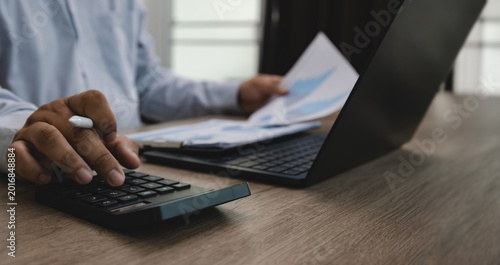 Photos Business person using calculator with financial documents and laptop on office desk, suitable for finance accounting, investment analysis, budgeting, expense calculation, and financial reporting