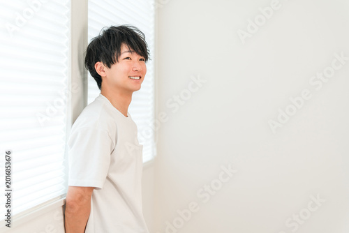 Obraz na płótnie A smiling Asian man in an oversized t-shirt is standing by the window