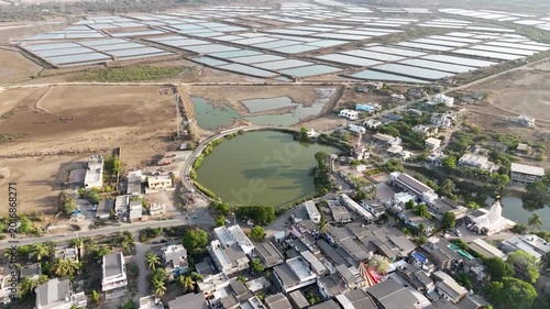 A breathtaking aerial view of expansive salt evaporation ponds spread across a dry coastal landscape near a rural village.