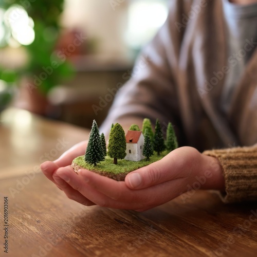 Woman Holds a Miniature House and Trees in Her Hands With a Smile Indoors