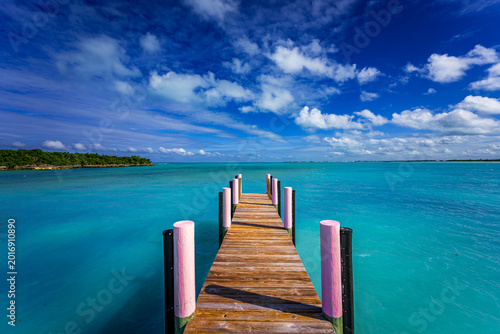 Принти на полотні Wooden pier stretching into crystal-clear turquoise water under a dramatic cloud
