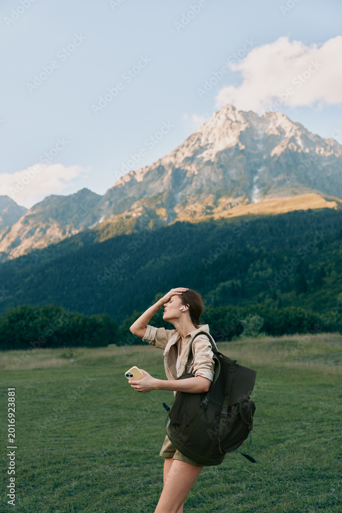 Naklejka premium Woman hiking outdoors with backpack, enjoying nature and mountain scenery, sunlit field, casual apparel, sense of adventure, travel, relaxed lifestyle, fresh air.
