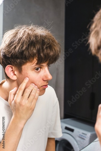Fotografi Teenage boy looking in the mirror and checking acne on his face