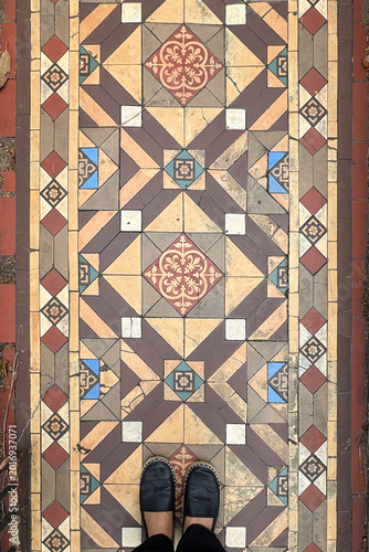 personal perspective of woman wearing black shoes standing on old mosaic tiled floor with detail pattern