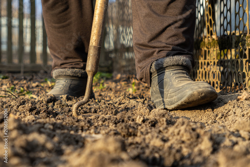 Konstfotografi Person wearing warm boots and trousers loosening soil with a manual garden hoe t