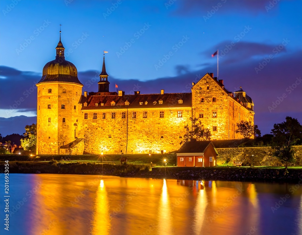 Fototapeta premium A large illuminated castle by a body of water at dusk