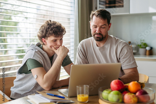 Cuadro en lienzo Father helping teenage son with diabetes with homework on laptop in kitchen
