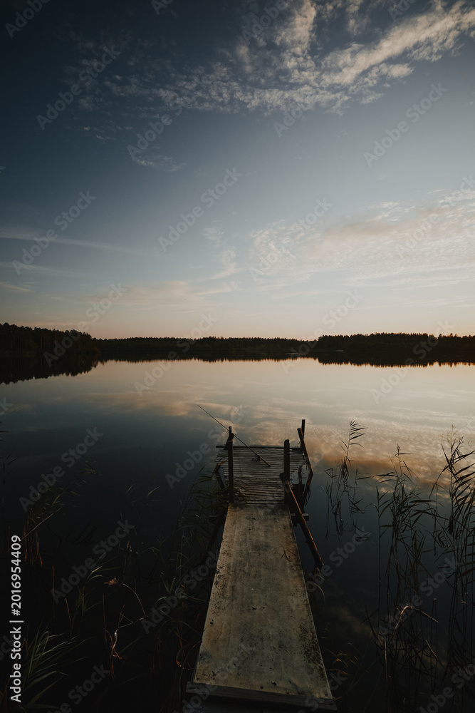 Fototapeta premium Fishing pier on a forest lake lit but the setting sun