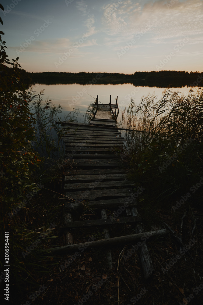 Fototapeta premium Fishing pier on a forest lake lit but the setting sun