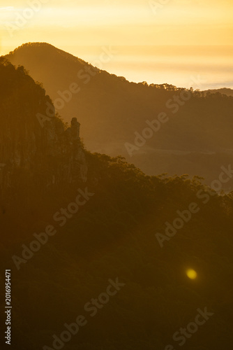 Schilderij op canvas Golden sunlight beaming over forest and mountains at sunrise