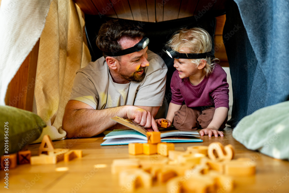 Fototapeta premium Dad and child building and reading book in cozy blanket fort.