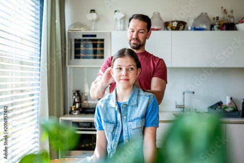 Tablou pe pânză Dad brushing daughter hair and making braid at home.