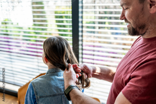Fotografie Dad brushing daughter hair and making braid at home.