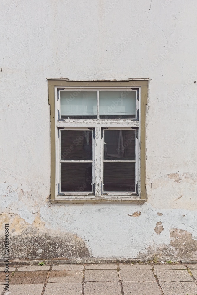 Fototapeta premium Traditional wooden casement window is set within a white stucco facade showing signs of age and deterioration, Saaremaa, Estonia, Europe.