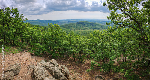 Wide southern panorama of rolling forested hills and dramatic storm clouds viewed from the Kövesdi lookout in the Bükk Mountains of Hungary.