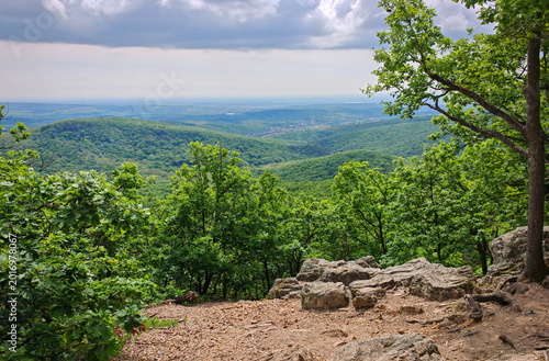 Rocky forest viewpoint overlooking green valleys and distant hills under dramatic spring clouds in the Bükk Mountains of northern Hungary.