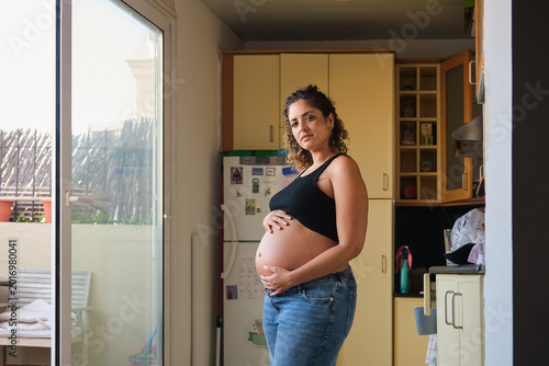 Quadro su tela Pregnant woman confidently cradling belly at home kitchen