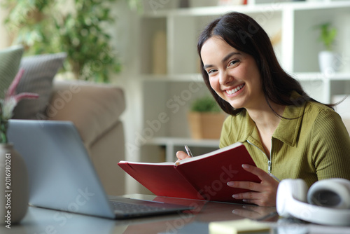 Happy student writing in agenda looking at camera