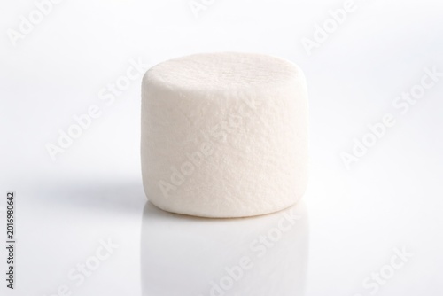 Single fluffy white marshmallow centered on a clean white reflective surface