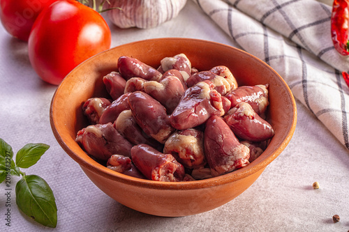 Canvas Print Fresh raw chicken hearts in a terracotta bowl surrounded by tomatoes, garlic, an