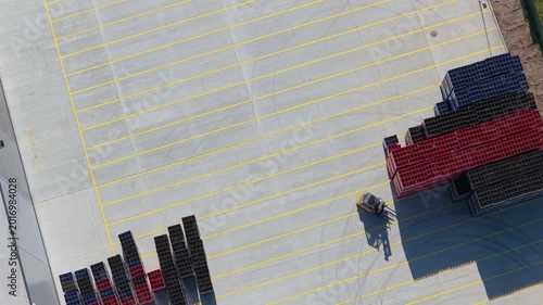 Top down view of forklift moving pallets in material warehouse yard, industrial logistics and supply chain distribution, aerial backward flight, 4K Cinematic