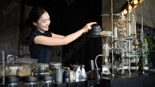 Canvas Print Happy young Asian barista skillfully brews specialty coffee using a gooseneck ke