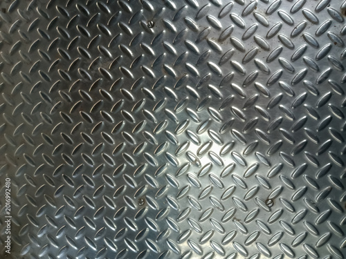 Abstract background a diamond plate, a type of metal sheet characterized by a regular pattern of raised diamonds or lines on one side. The surface is metallic and reflective