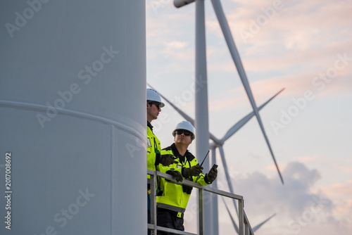 Foto Diverse industrial technicians with tablet and walkie-talkie inspecting wind farm during evening shift, green energy concept