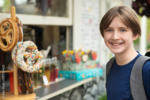  Portrait of a smiling boy with backpack standing near traditional pretzels display in outdoor market