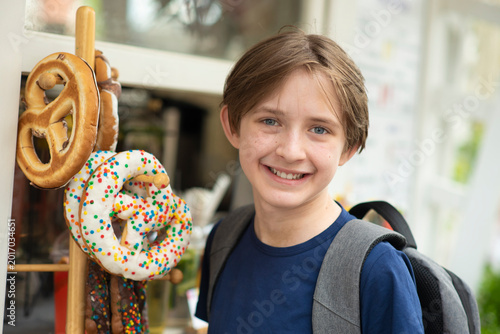  Portrait of a smiling boy with backpack standing near traditional pretzels display in outdoor market