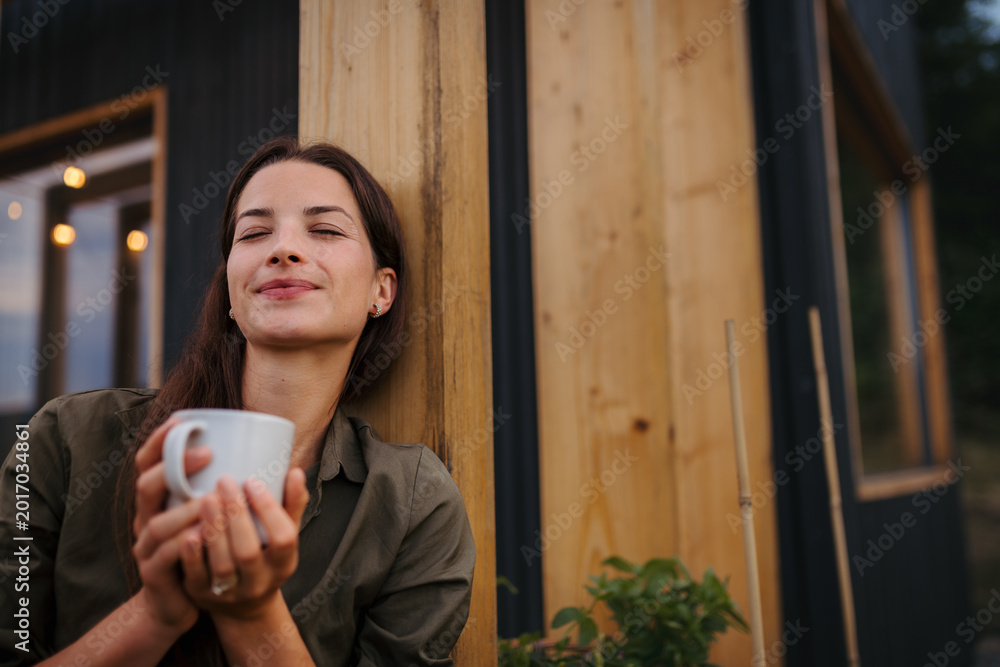Fototapeta premium Young woman with coffee outdoors, weekend away in container house in countryside.