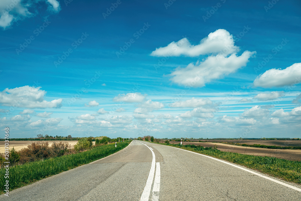 Obraz premium Open country road under blue sky with white clouds stretching across flat landscape