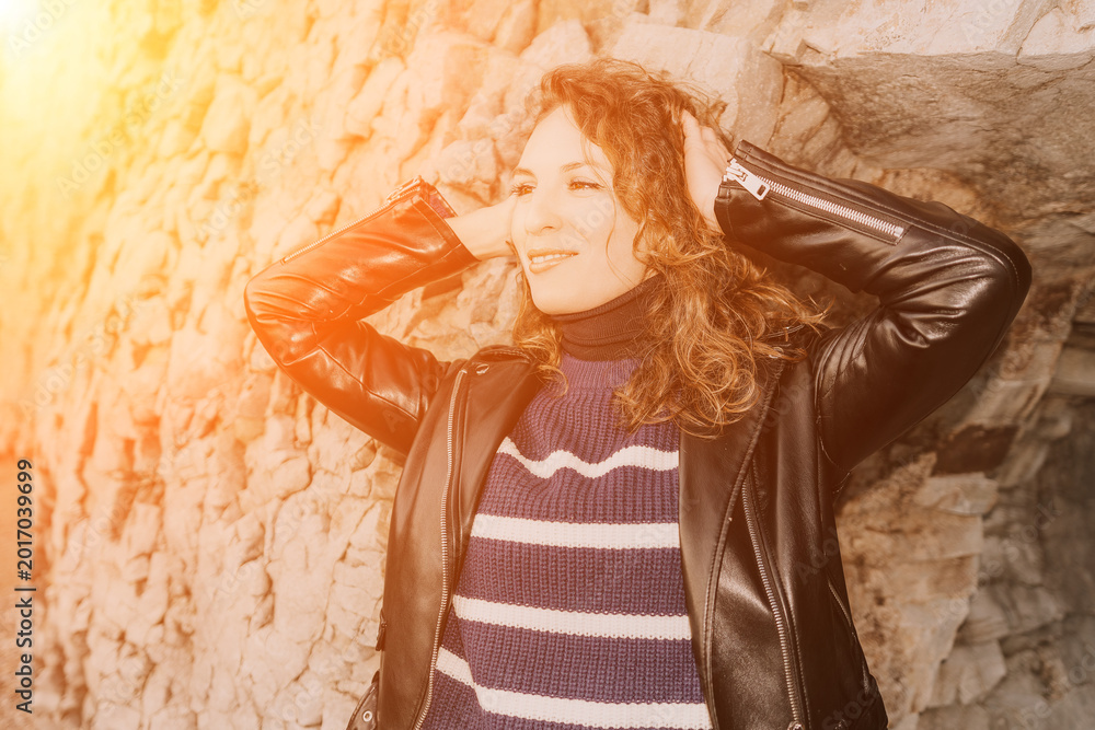 Obraz premium Woman leather jacket portrait posing against stone wall in bright sunlight for fashion and lifestyle concepts