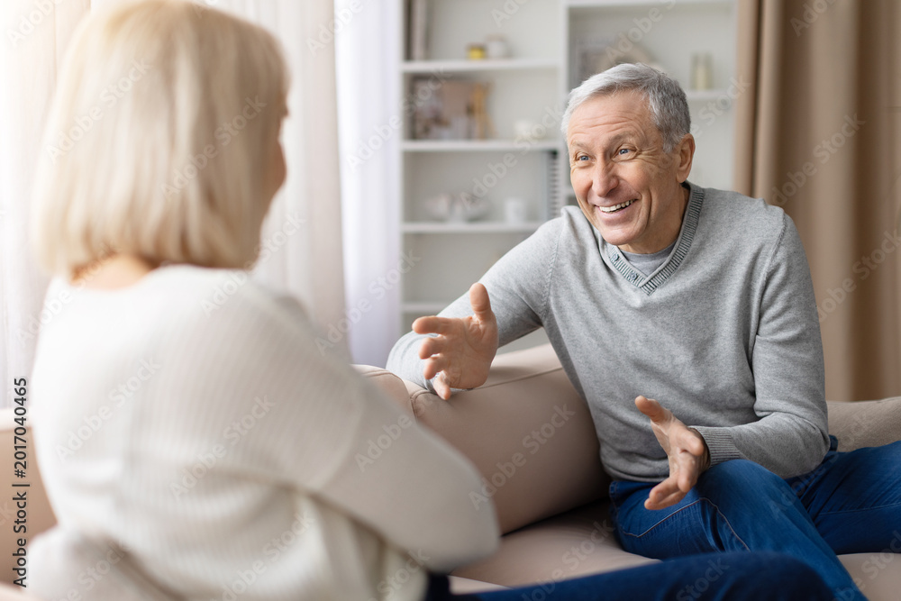 Obraz premium Emotional senior man gesturing during conversation with mature woman at home, expressing strong feelings in domestic relationship discussion scene