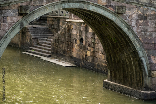 Foto Ancient stone arch bridge framing a historic canal with weathered masonry walls and stone steps