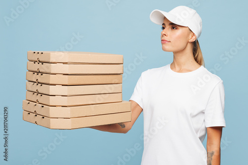 Delivery employee woman wear white cap T-shirt uniform workwear work as dealer courier hold pizza in cardboard flatbox isolated on plain pastel light blue background studio portrait. Service concept.