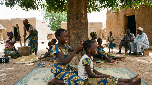 African Children Bonding in Village Under Tree, One Braiding Hair