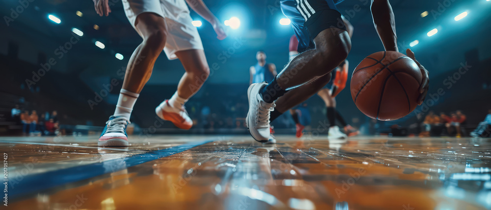Naklejka premium Professional basketball player dribbling ball on indoor court under bright arena lights. Dynamic sports action scene showing strength, focus, competition and high intensity athletic performance.