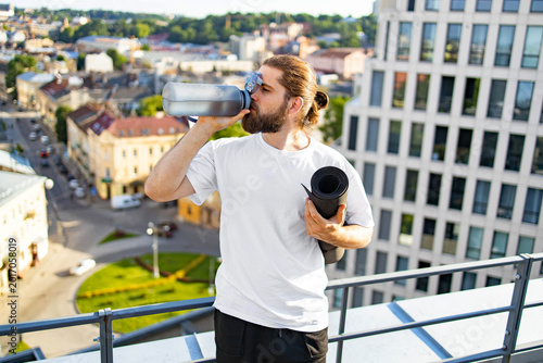 Foto A bearded man with his hair in a bun drinks from a large water bottle while hold