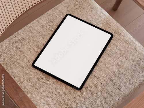 Blank screen tablet placed on a beige fabric chair seat.