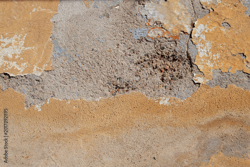 Peeling yellow plaster wall texture with exposed concrete and weathered paint...