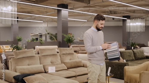 Man considering fabric swatches for sofa upholstery in modern furniture store showroom, home improvement shopping